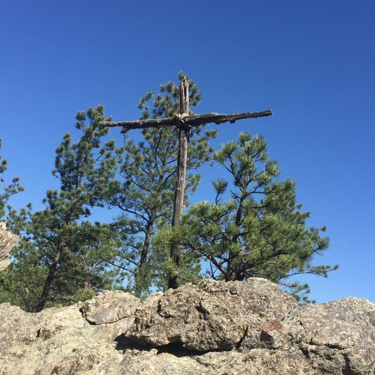 rugged cross on rocks surrounded by pine trees